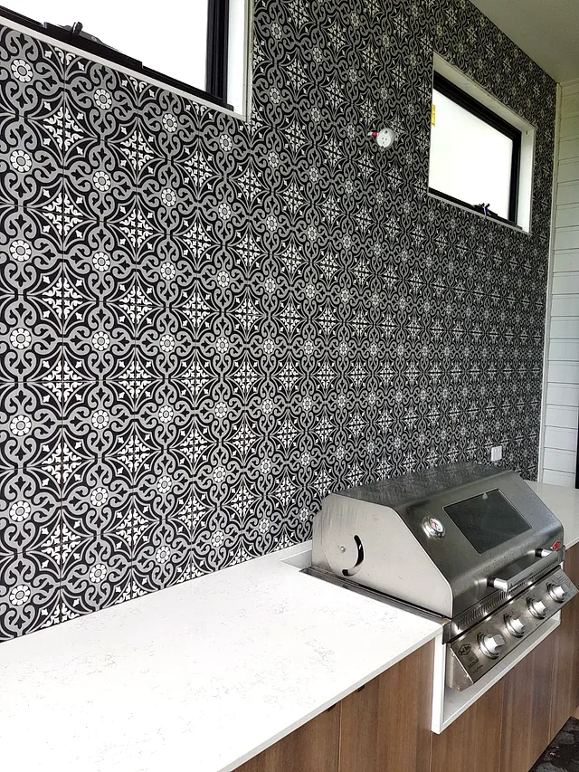Black-and-white patterned feature wall tiles behind an outdoor barbecue and bench