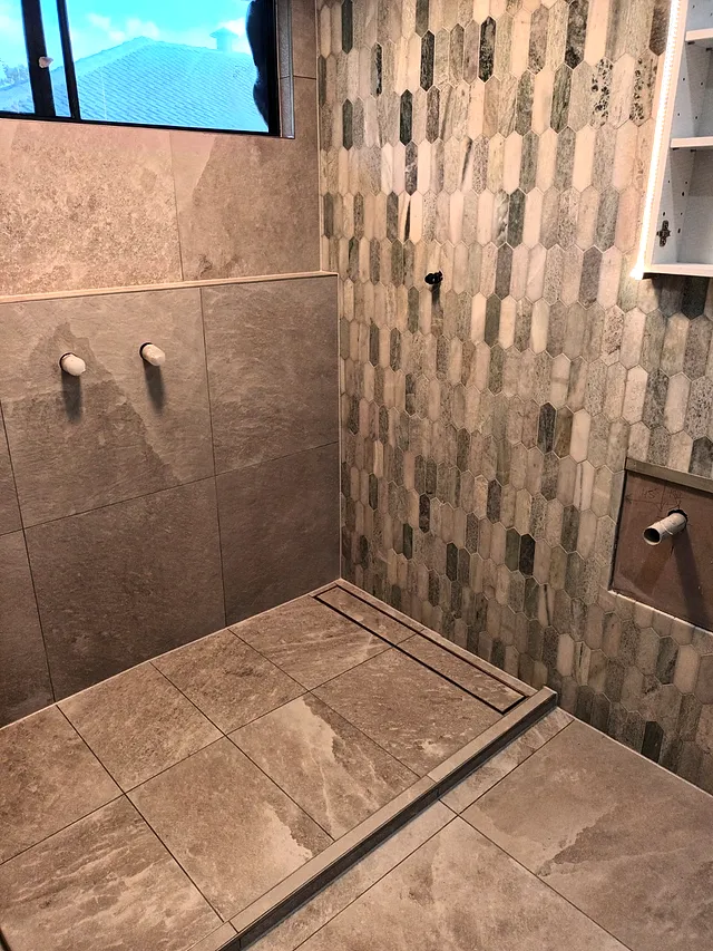 Shower with textured feature tiles, a vertical mosaic wall, niche and linear drain
