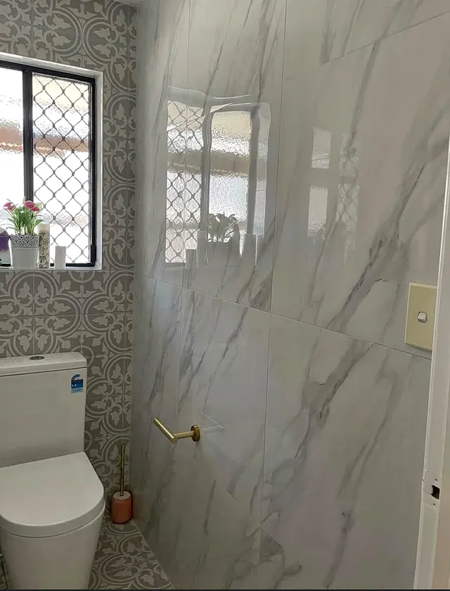 Toilet room with marble-look wall tiles, patterned floor tiles and brass fittings