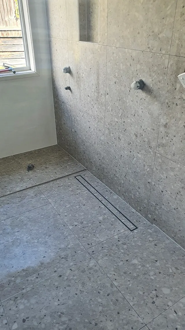 Shower with terrazzo-look wall and floor tiles and a linear drain