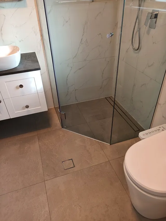 Glass shower next to a floating vanity and toilet with large floor tiles