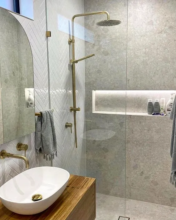 Bathroom with a brass rain shower, arched mirror, timber vanity and a lit niche behind glass
