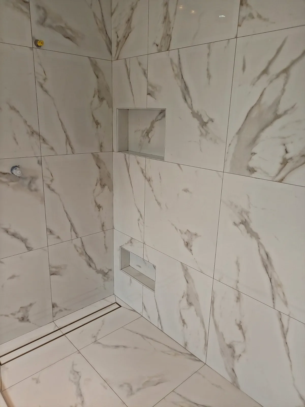 Marble-look shower with two recessed niches and a linear floor drain