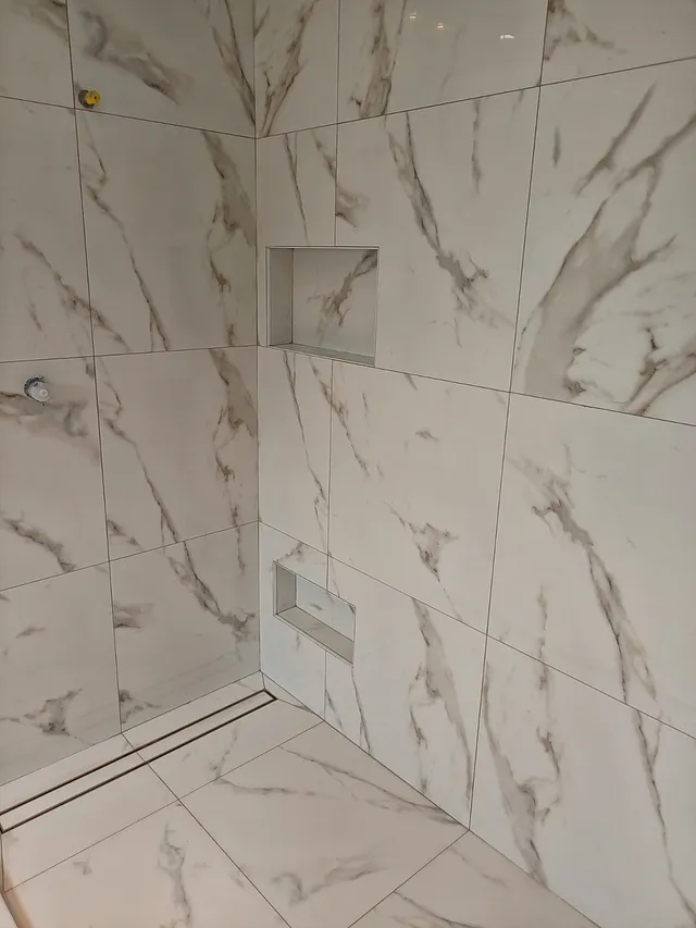 Shower with marble-look large-format wall tiles, two recessed niches and a linear floor drain