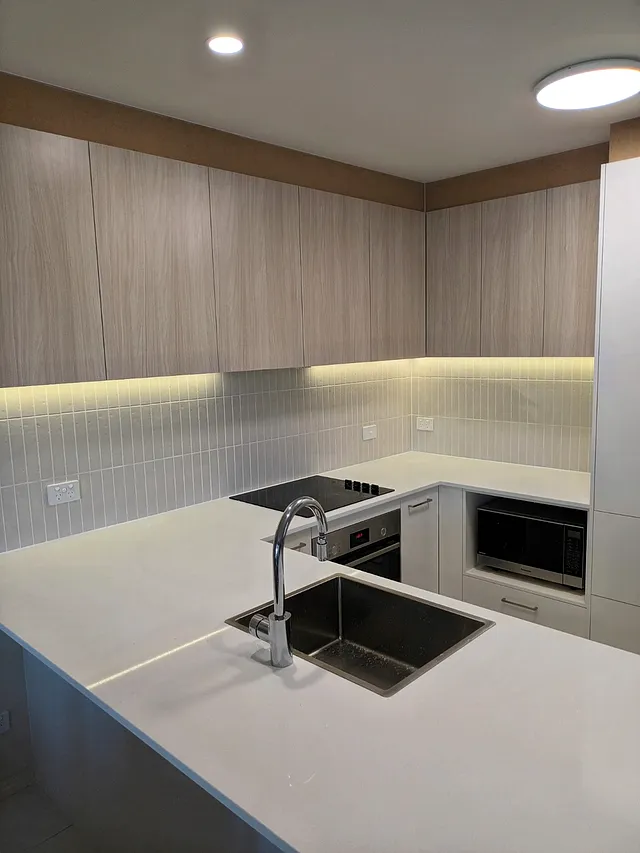 Kitchen with pale cabinets, a light textured splashback and under-cabinet lighting