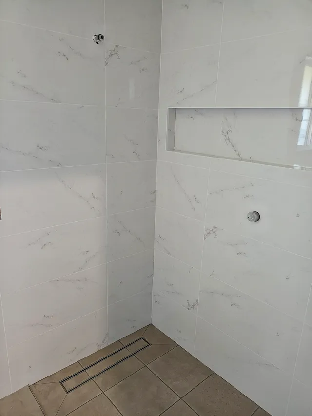 Marble-look shower walls with a long recessed niche and linear drain
