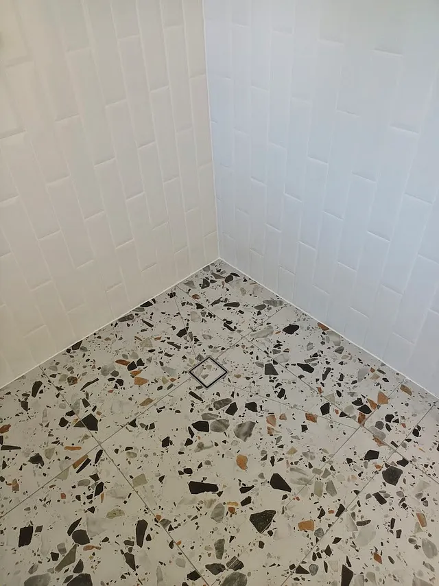 Terrazzo floor tiles and white feature wall tiles in a shower recess