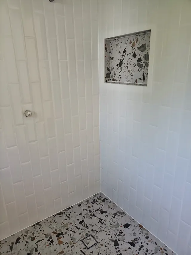 Shower with white vertical wall tiles, a terrazzo-look niche and terrazzo floor