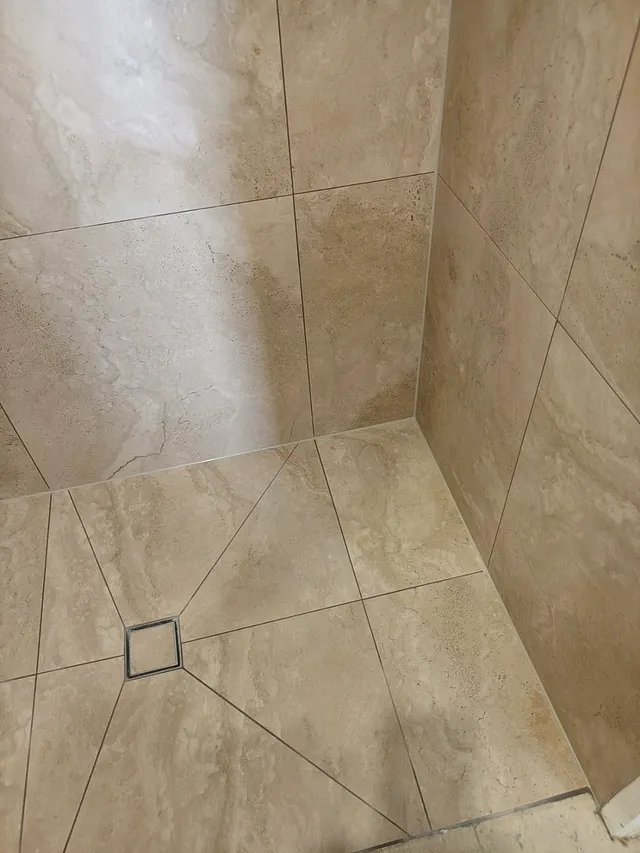 Shower with large-format beige wall and floor tiles and a square drain