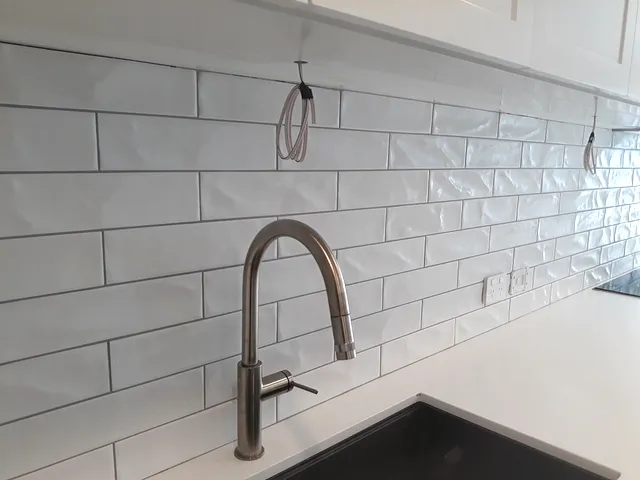 Long white textured subway tile splashback behind a kitchen sink and mixer tap